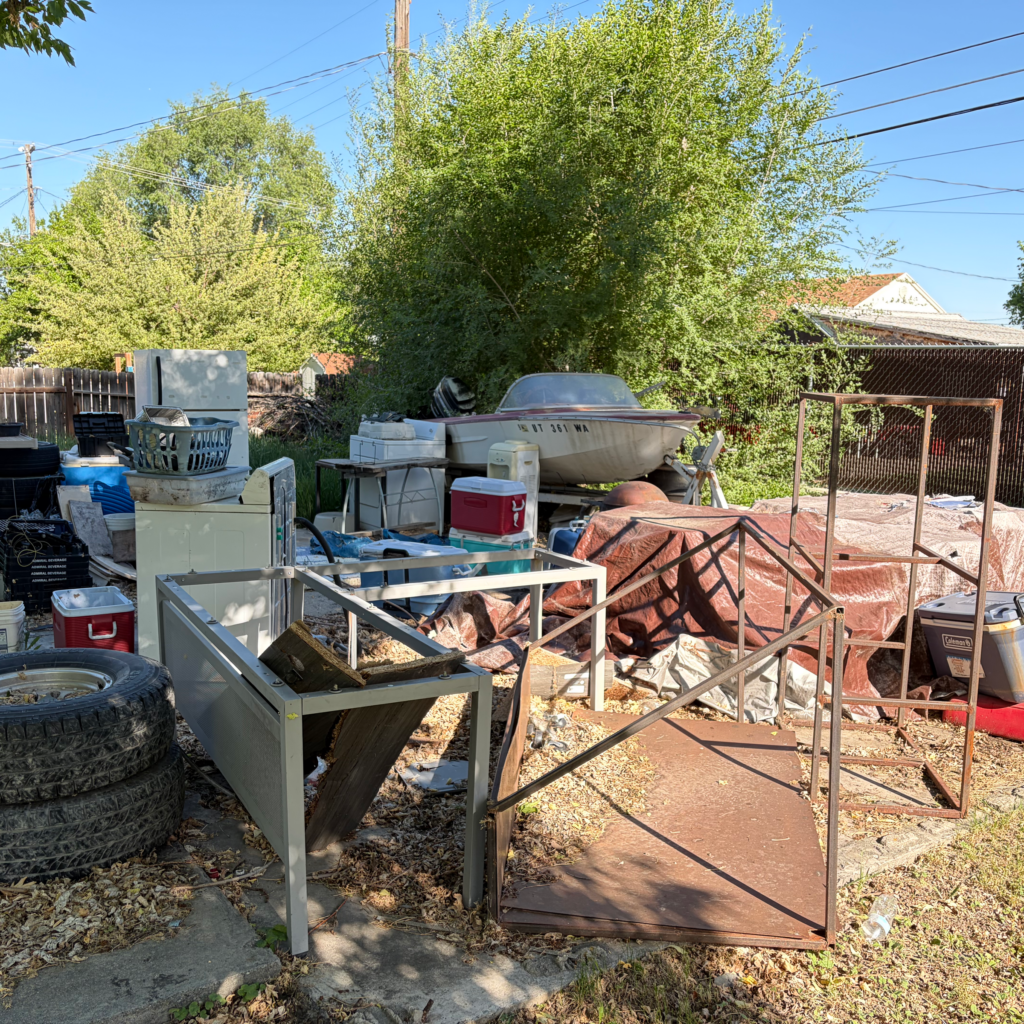 Backyard cleanout with scrap metal frames, tires and an old boat before removal